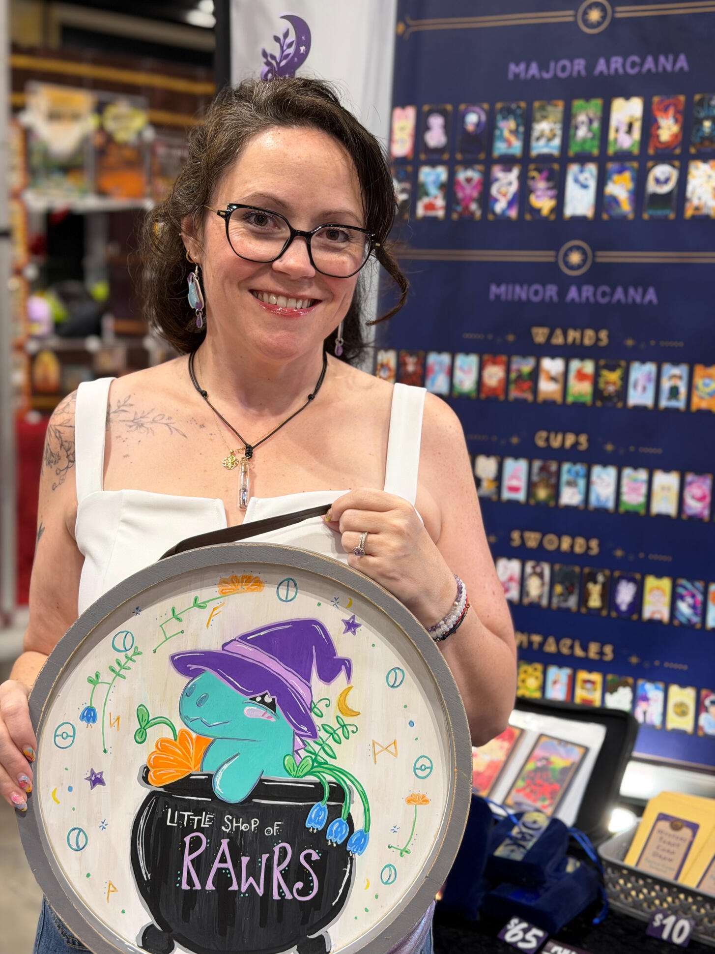 Heather at her Little Shop of RAWRS convention booth Heather smiling at her Little Shop of RAWRS convention booth, surrounded by Pokemon art prints and stickers